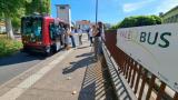Des passagers montant dans le véhicule autonome, une petite navette rouge, dans une rue ensoleillée. le public prend des photos devant un panneau indiquant PaléoBus.
