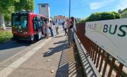 Des passagers montant dans le véhicule autonome, une petite navette rouge, dans une rue ensoleillée. le public prend des photos devant un panneau indiquant PaléoBus.
