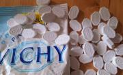 Un paquet de pastilles de Vichy ouvert sur une table en bois, des dizaines de pastilles blanches octogonales marquées Vichy ou 200 ans