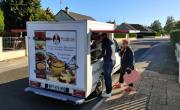 un camion de vente ambulante installé dans une rue. une femme âgée avec son cabas regarde les produits devant l'étal du camion, ouvert sur le côté. l'arrière du véhicule est floqué avec de illustrations de nourriture et le logo Patifrais