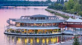 Sous une lumière rosée de fin de journée, la rotonde éclairée au milieu du lac d'Allier une passerelle la relie à la rue, on distingue les deux étages