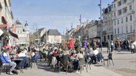 Des gens son assis en terrasses au milieu d'une grande place bondée, le ciel est bleu