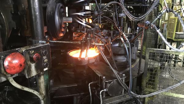 On voit des machines industrielles avec des fils, boutons, tuyaux et du verre en fusion au centre d'un moule d'isolateur